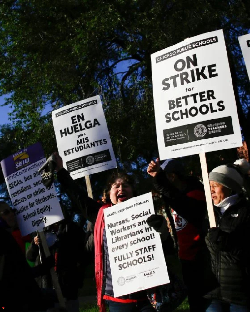 A group of people holding protest signs, including messages in English and Spanish, outside a building, advocating for better schools and staffing.